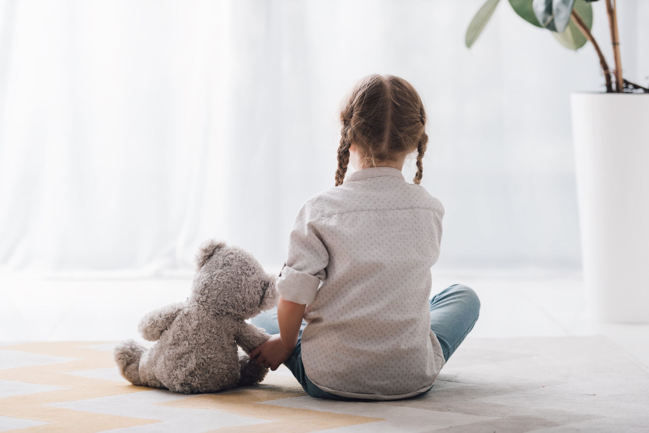 rear view of little child sitting on floor with her teddy bear t