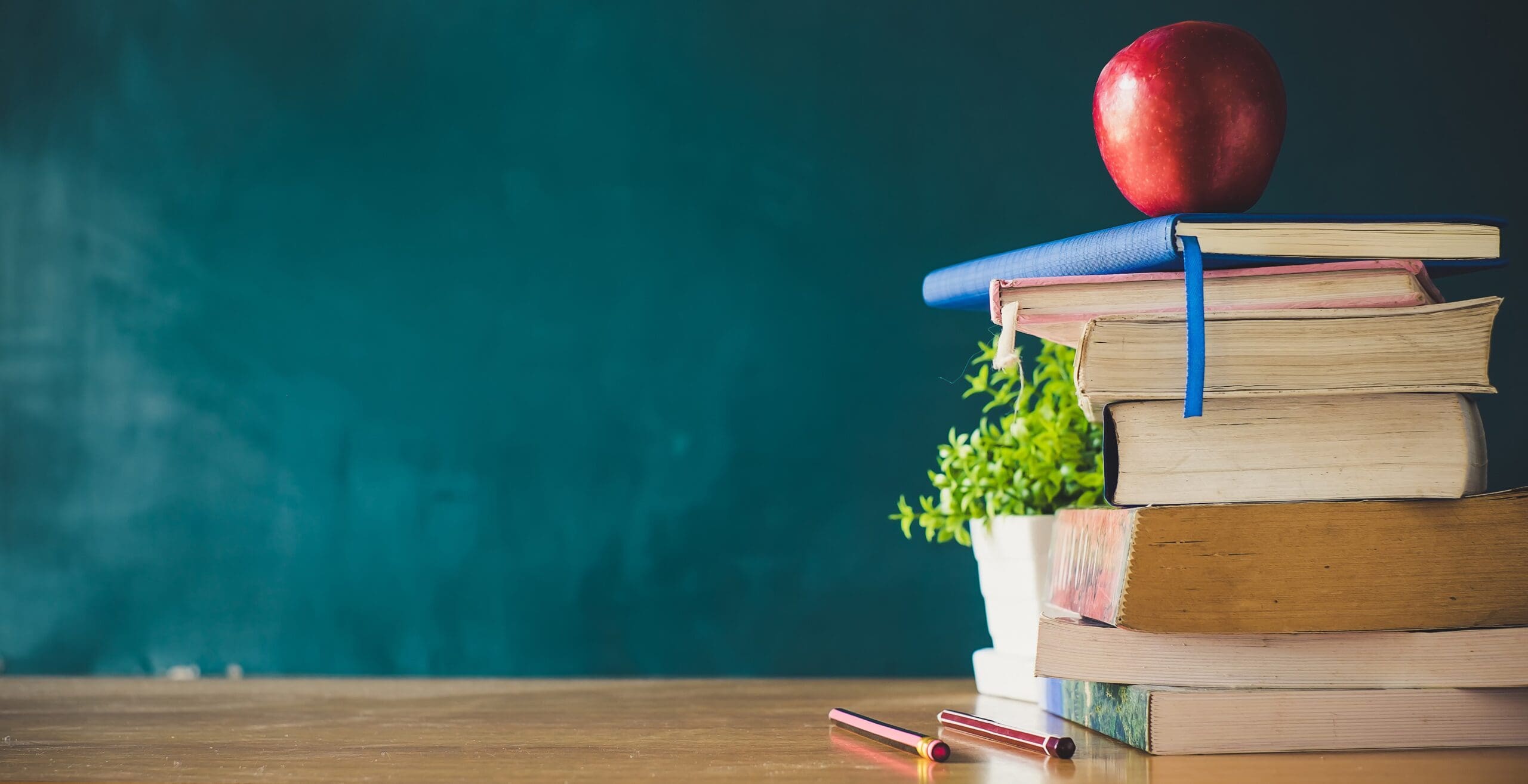 School books with red apple on desk over green school board background