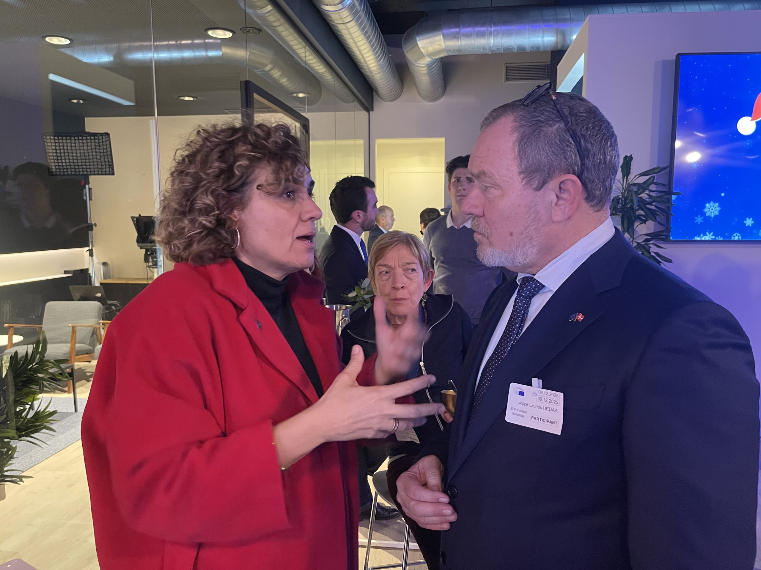 Jeppe Hedaa, formand for KristenDemokraterne, i samtale med Dolors Montserrat, generalsekret&aelig;r for EPP (European People's Party), ved et EPP-arrangement. I baggrunden ses &oslash;vrige deltagere i et moderne m&oslash;delokale.