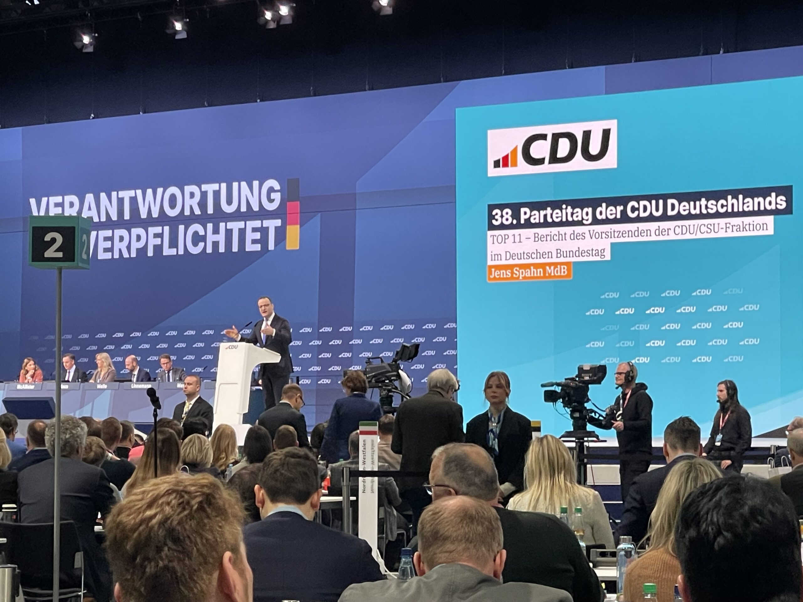 Stor konferencesal med en taler p&aring; talerstolen, p&aring; bagv&aelig;kken et stort CDU logo.